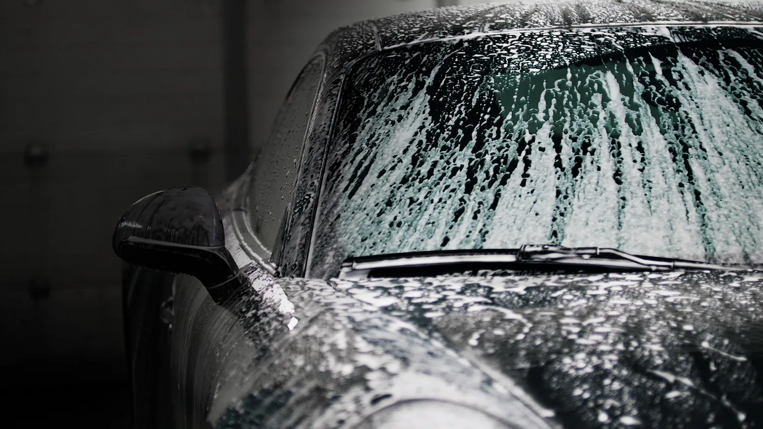 Water beading on a dark car windshield, illustrating care and cure time after windshield film install