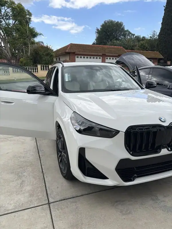 Alpine White BMW X1 M-Sport front three-quarter view with driver door open after front 2-window ceramic IR tint install — BestAutoTechs San Diego mobile service